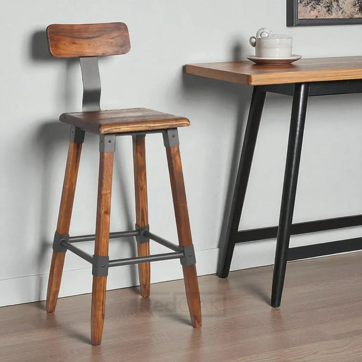 Wooden bar stool with metal accents next to a wooden table against a white wall.