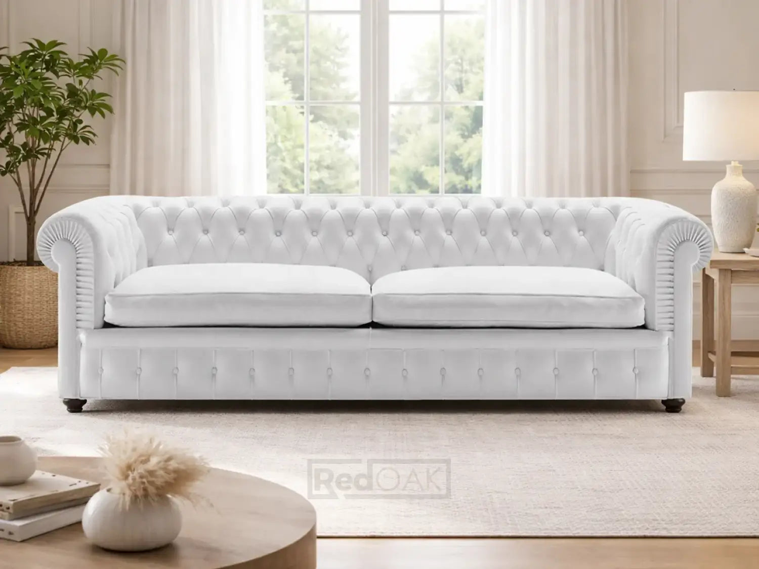 White tufted chesterfield sofa in a living room with a lamp, plant, and coffee table.