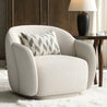 White armchair with a patterned pillow in a room setting with a wooden table and lamp.