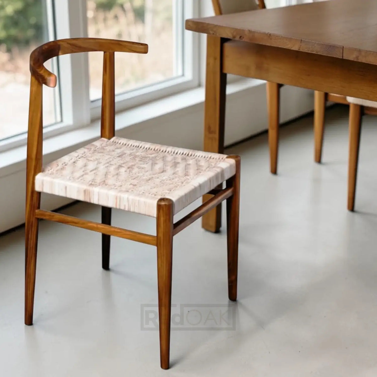 Wooden chair with woven seat in a room with a table and windows.