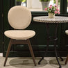 Beige chair next to a small round table with a floral arrangement in an indoor setting.