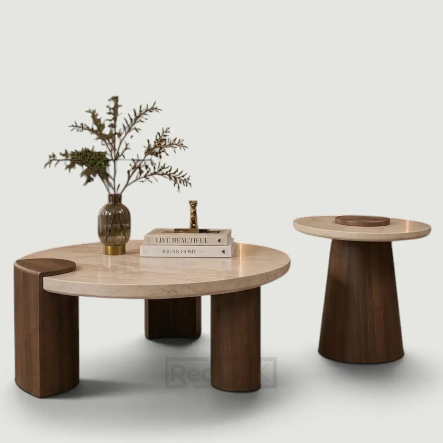 A modern round coffee table with a light natural wood top and dark brown block legs, styled with a vase of branches and books, alongside a matching smaller side table on a light gray background.