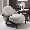 Beige armchair with black legs in a room setting with a table and lamp.