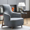 Gray armchair in a modern room with a lamp and books on a shelf.