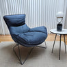 Blue lounge chair in a room with a white curtain and small round table.