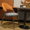 Chair with orange backrest and gray cushion next to a table with a cup and flowers.