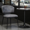 Gray upholstered chair next to a small round table with a drink in a cafe setting.